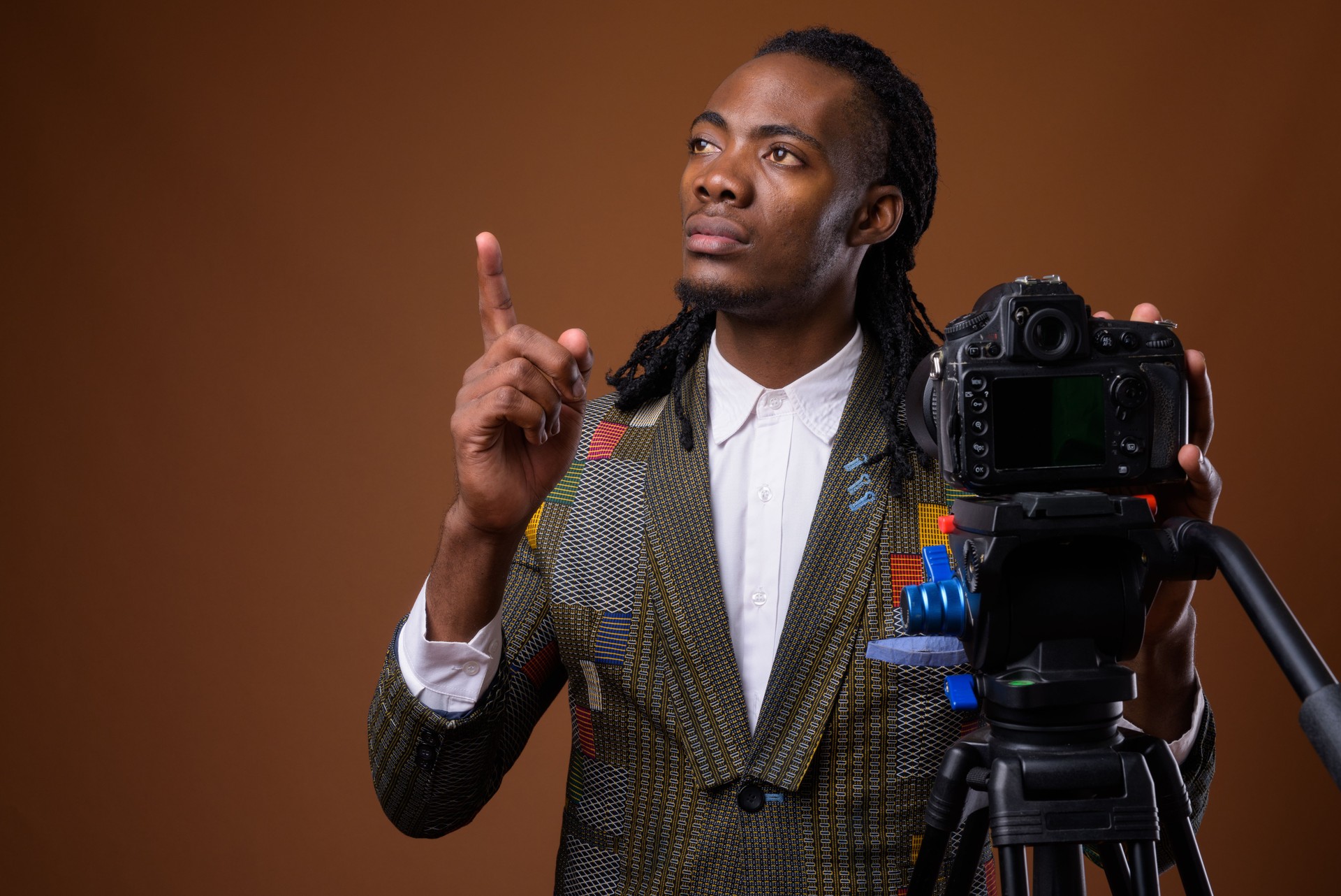 Studio shot of young handsome African businessman getting ready for vlogging against colored background